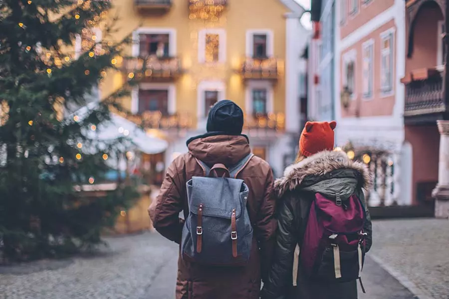 Young couple walking around a winter mountain village, wearing warm clothes and backpacks.